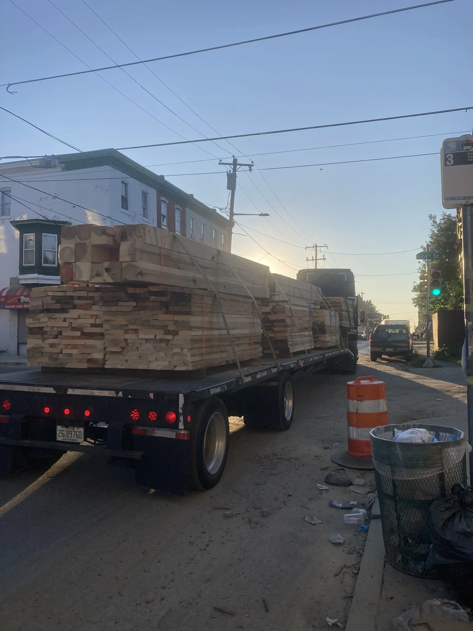 A flatbed truck carrying large stacks of lumber on a city street during sunset.
