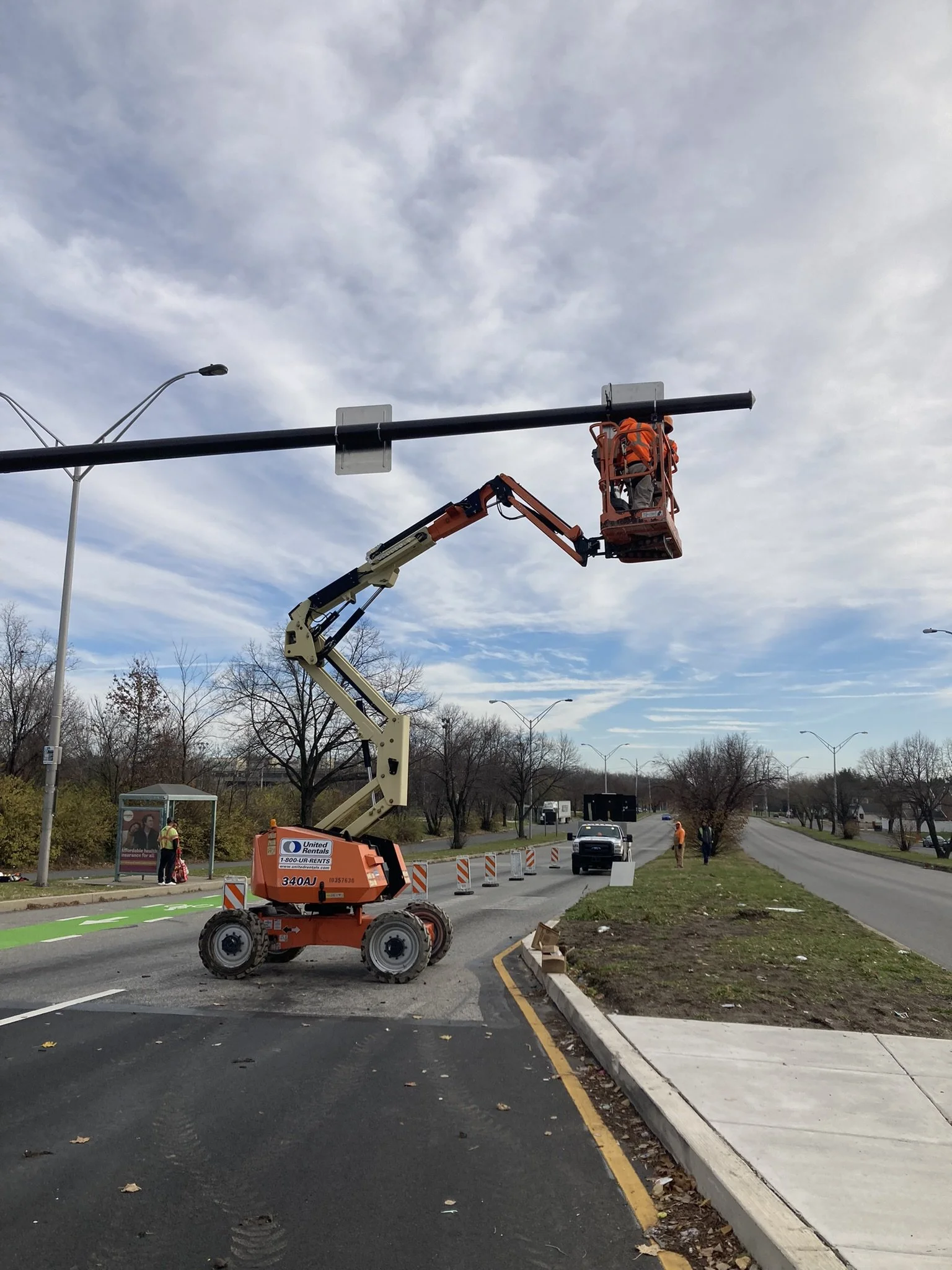 A worker on a cherry picker installs or repairs a street light on a busy road.