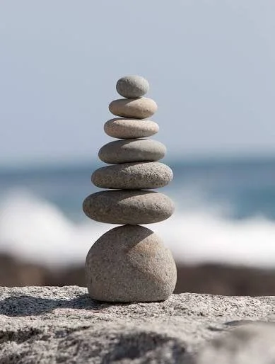 Stacked smooth rocks balanced on a larger rock near the ocean with waves in the background.