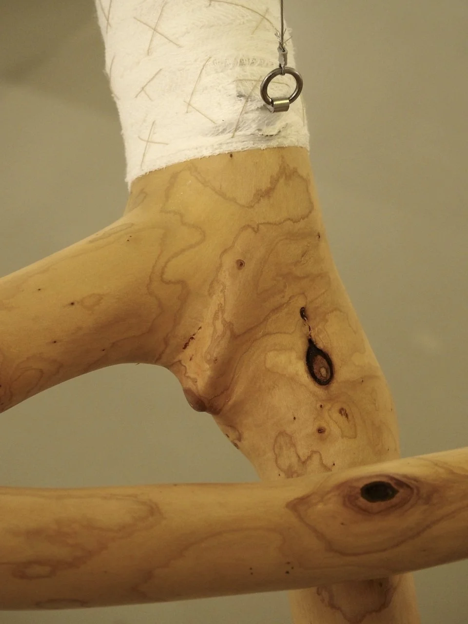 Close-up of a wooden object with a white cloth wrapped around the top, a metal ring hanging from the cloth, and visible wood grain and knots.