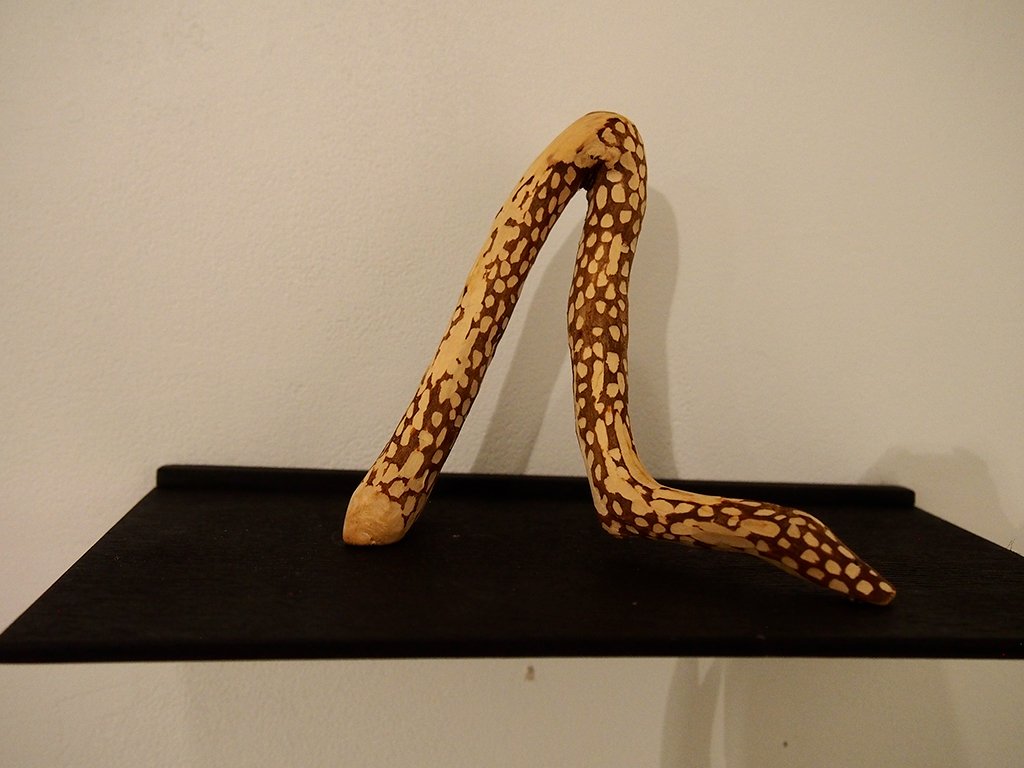 A decorative object resembling a snake with a yellow and brown patterned surface, positioned on a black shelf against a white wall.