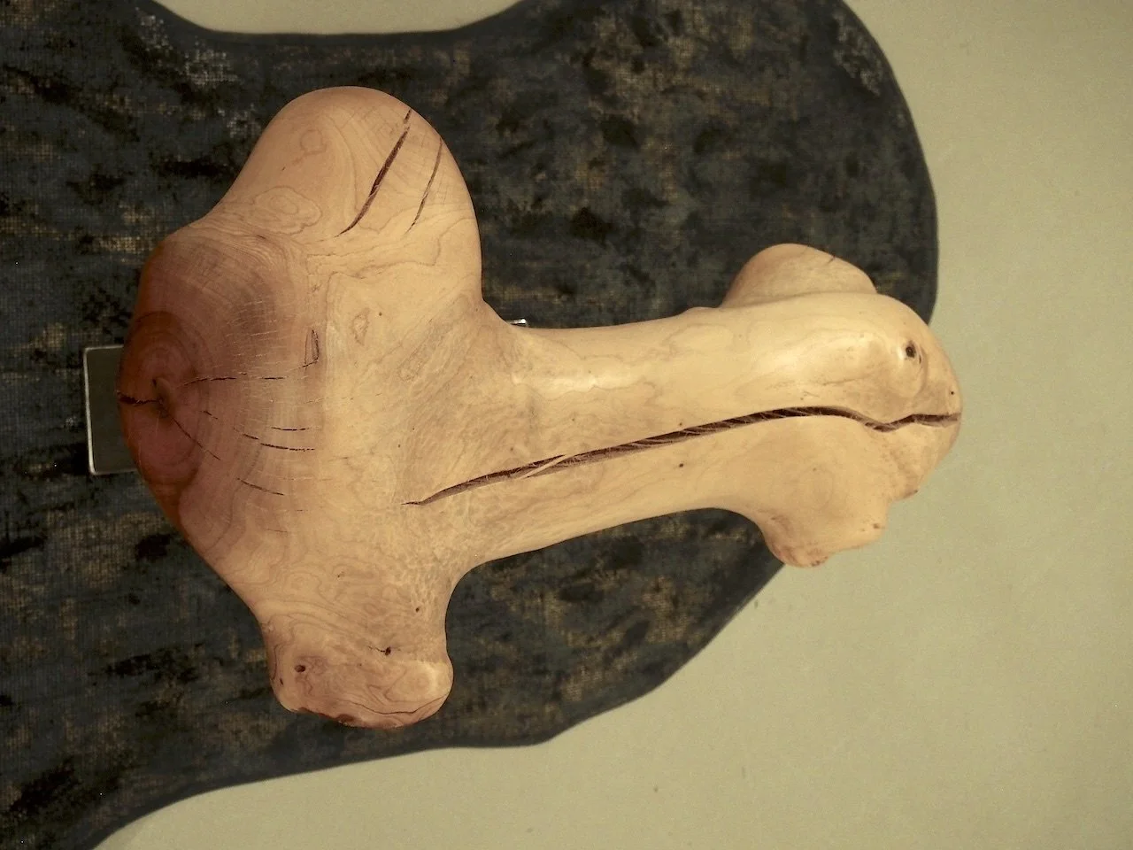 Wooden sculpture shaped like a dog with pronounced ears and a long neck, displayed on a dark surface.
