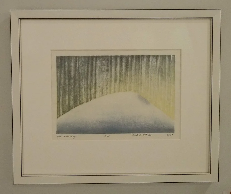 A framed and matted abstract art piece featuring a stylized, curved shape with vertical lines in the background, blending shades of green, yellow, blue, and gray.