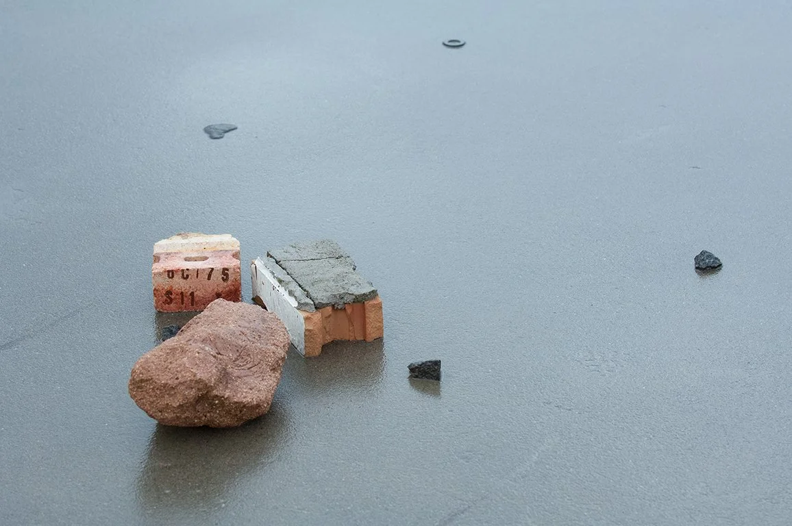 Small rocks and bricks scattered on a smooth gray surface.