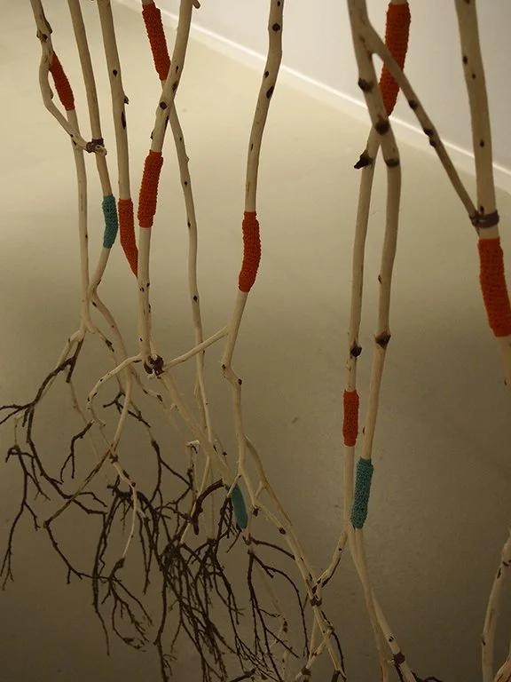 Decorative branches with colored yarn wrapped around them, arranged vertically indoors.