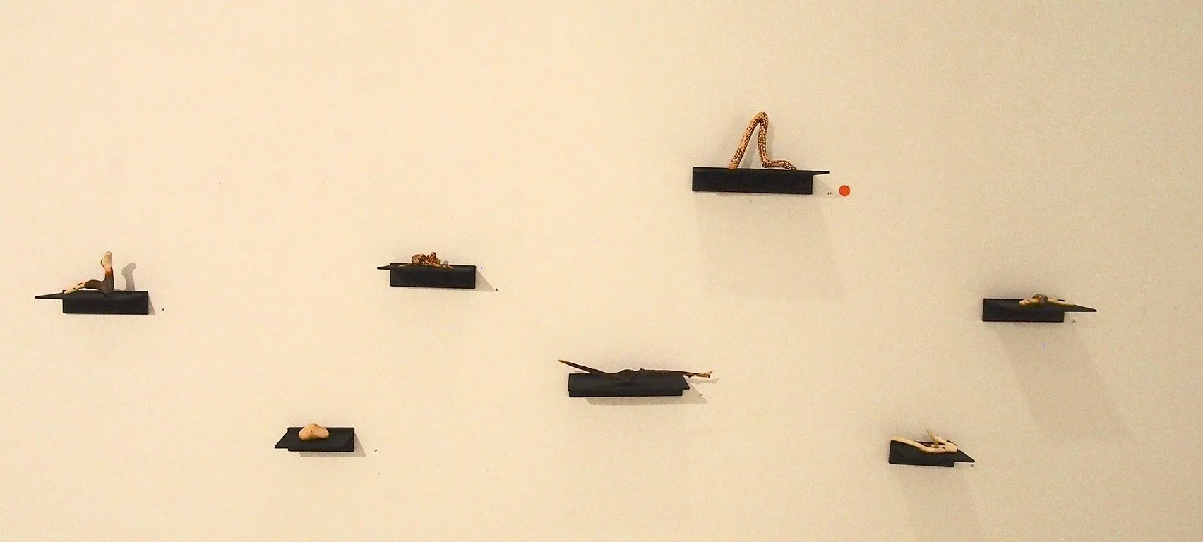 Small sculptures of insects displayed on black wall-mounted platforms on a plain white wall.