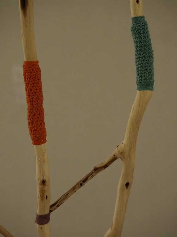 Wooden sticks with colorful yarn wrapped around sections, set against a plain background.