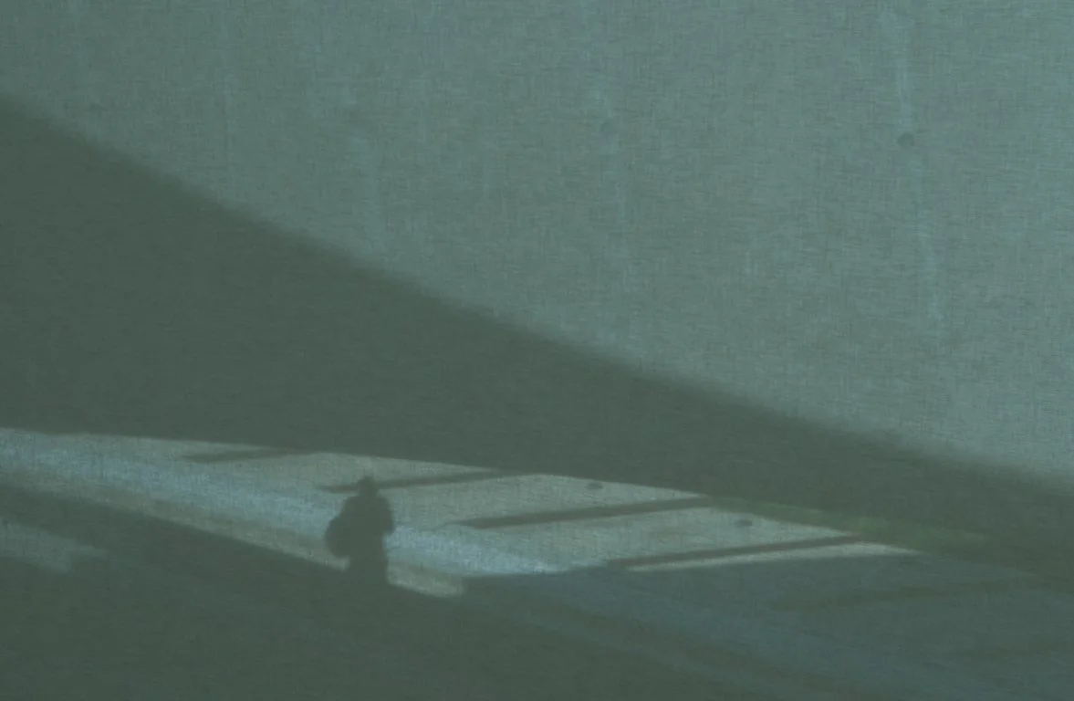 Shadow of a person on a textured wall with a partial view of a window or opening.