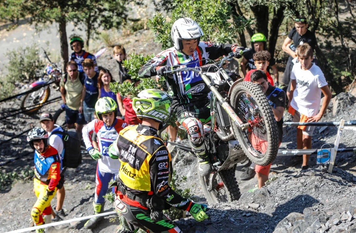 モーターサイクルの選手が岩場のコースを登坂している様子と、観客が見守っている場面