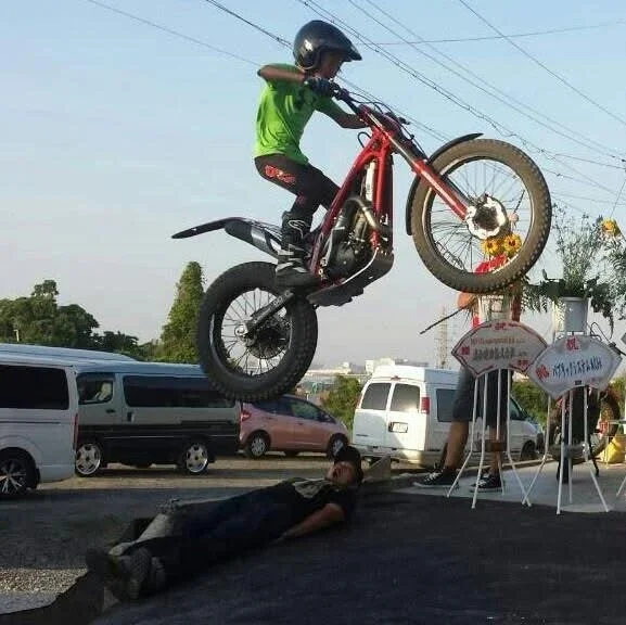 側面でバイクジャンプをしている少年と、地面に寝ている少年がいる道路の風景。
