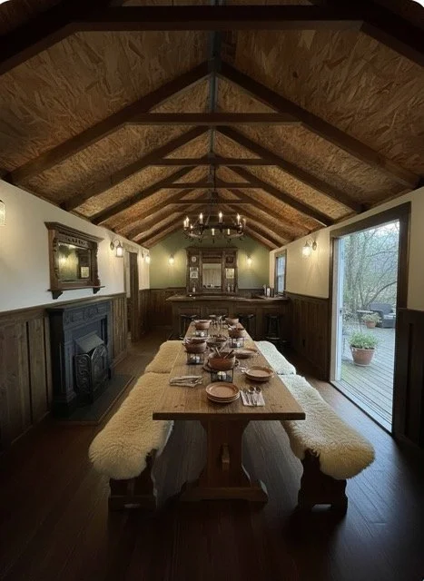 A rustic dining room with a wooden ceiling, long wooden table set with dishes and glasses, a chandelier, large windows, and a sliding glass door leading outside.