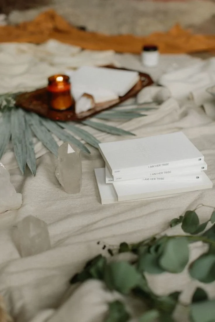 A tabletop display with candles, books titled "I AM HER TRIBE," crystals, plants, and other decorative elements with a boho aesthetic.