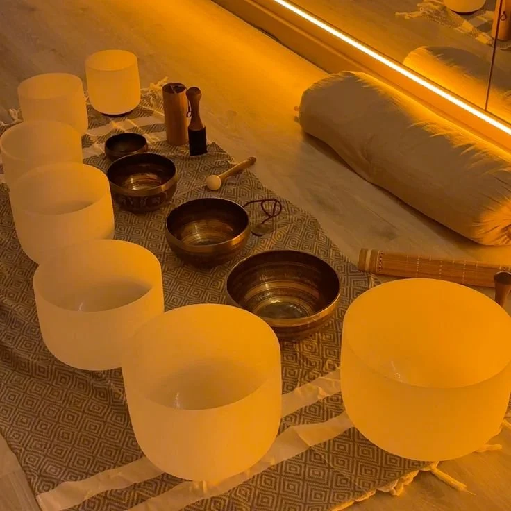 A collection of crystal singing bowls arranged on a decorative cloth with a wooden mallet, set in a warm lit room.
