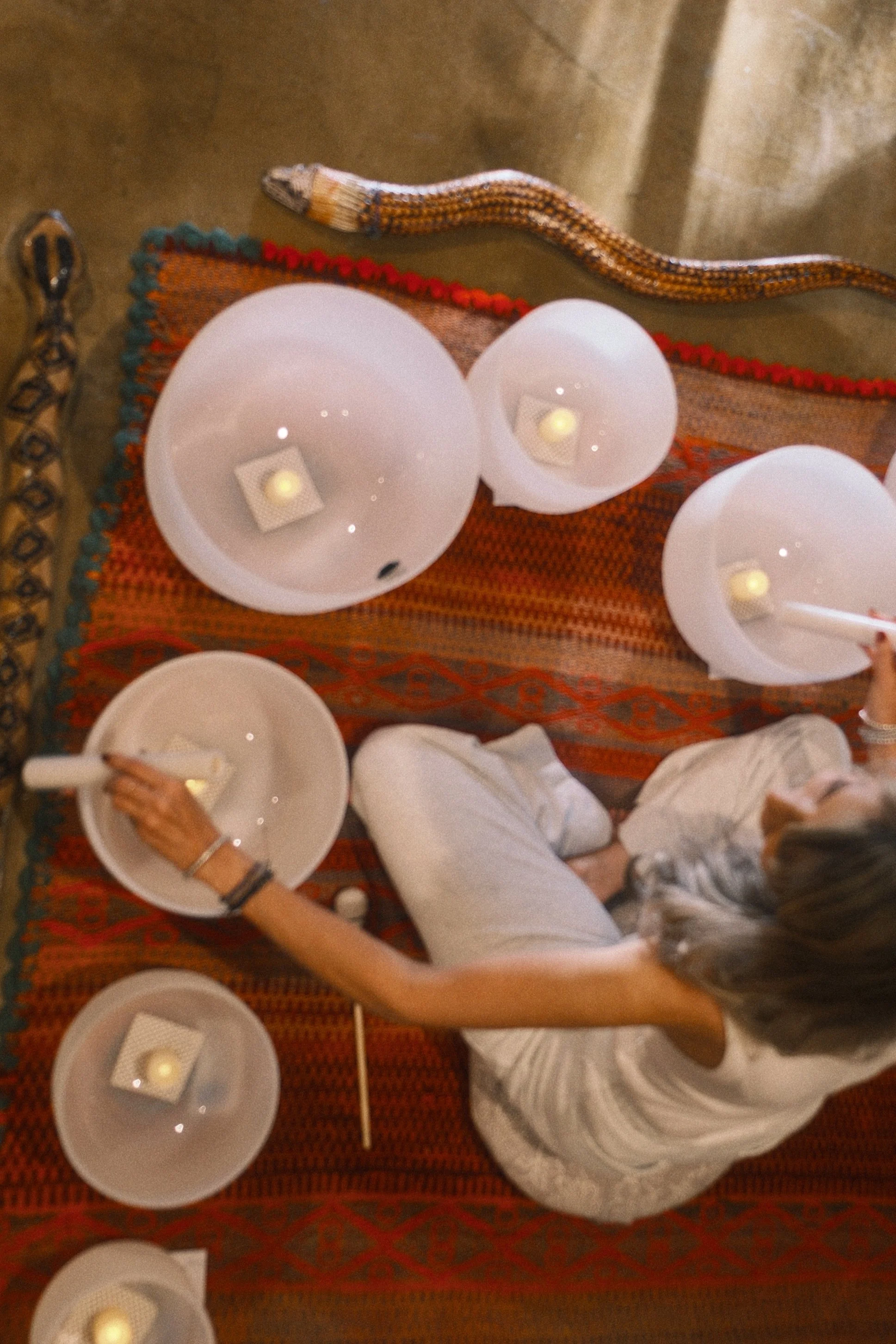 A snake on a carpet, next to a woman in white, who is reaching for a plate with napkins and a lit candle inside a grainy photo.