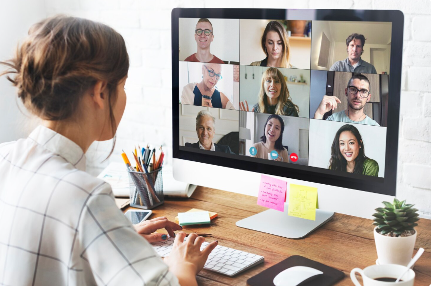 Woman participating in a virtual meeting on a computer with eight diverse people in video call.