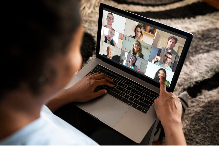 A woman participates in a video conference on a laptop, showing multiple people in a grid layout on the screen.