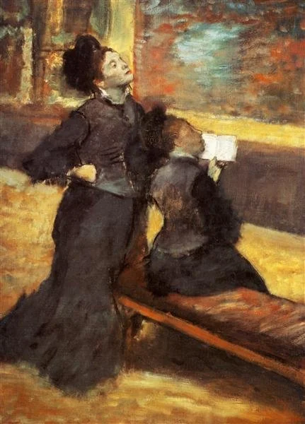 Two women with dark hair, one standing and one sitting, in a room with warm, glowing lighting. The standing woman is looking upward, and the sitting woman is reading a book.