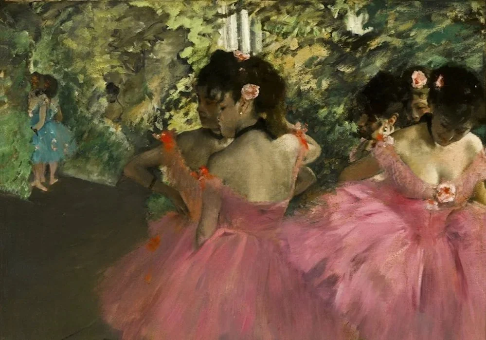 Three women in pink ballet costumes dancing and posing outdoors with a green leafy background, one girl in the background on the left wearing a blue dress.