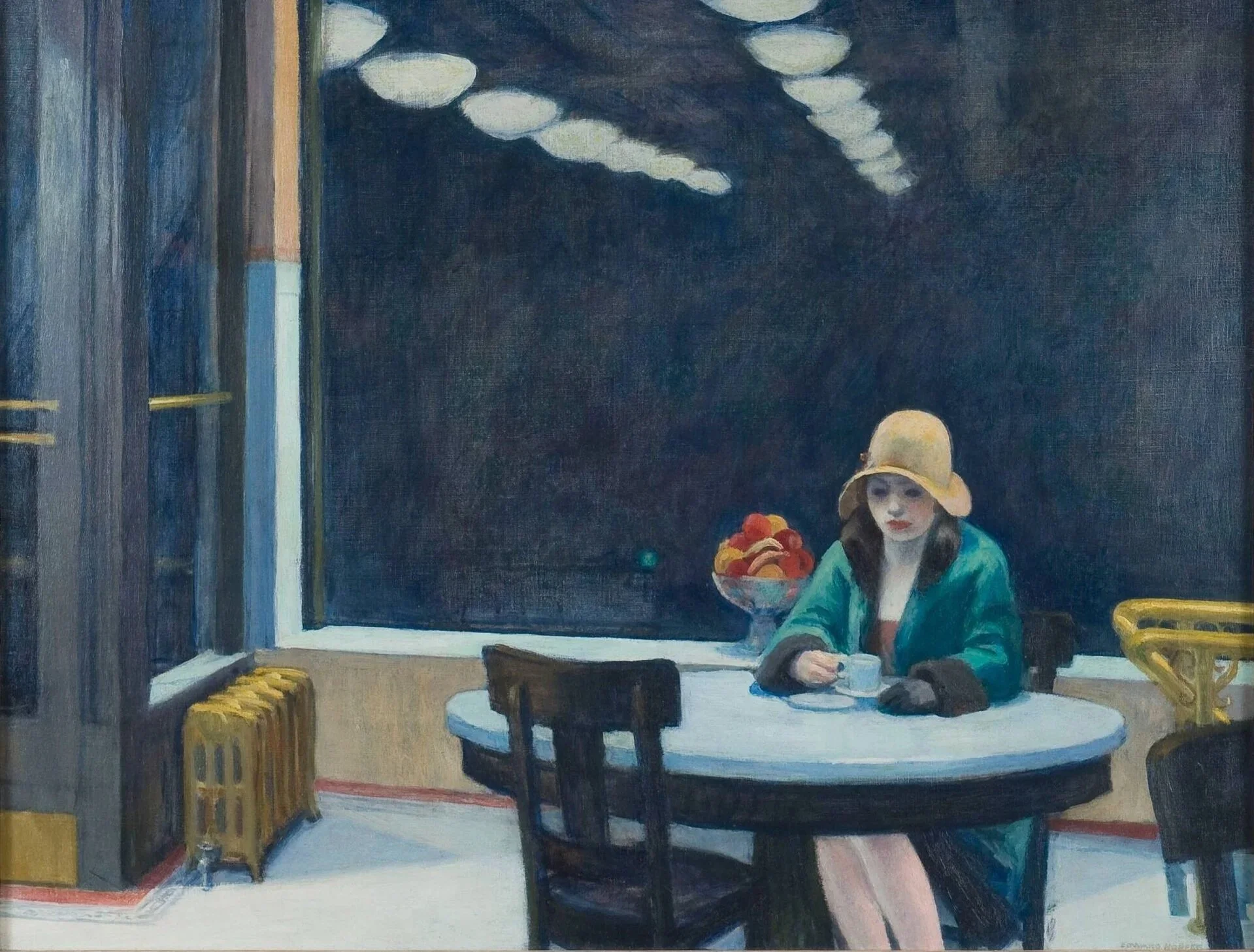 A woman with dark hair wearing a yellow hat and teal jacket sits at a white table, looking down and holding a bowl, with a bowl of fruit on the table. The background features a dark window, and a yellow stool is visible beside her.