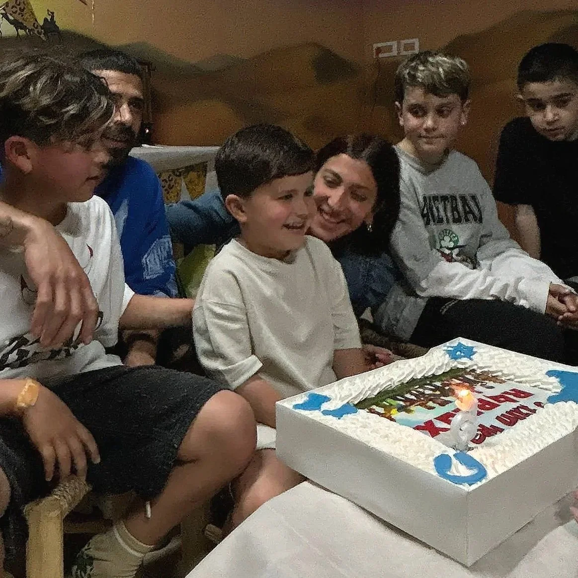 Group of children and an adult sitting around a birthday cake, celebrating with smiles.
