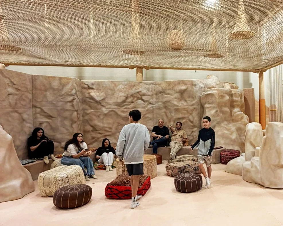 Group of children and adults sitting and standing in a cave-like room with large rock formations, lounge seating, and cushions.
