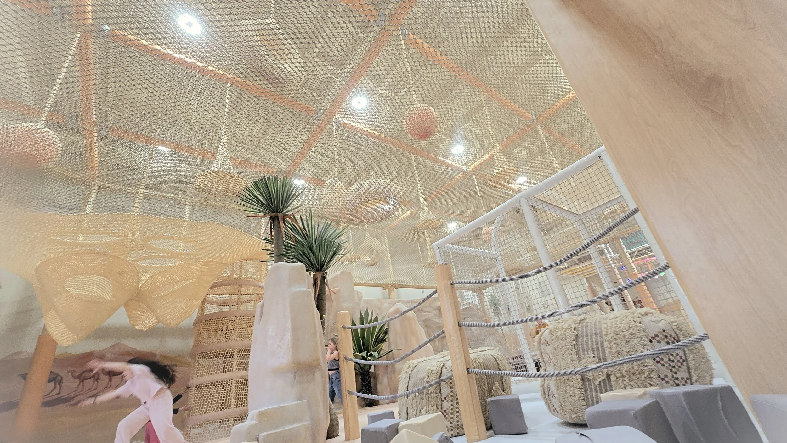 Interior of a playful area with a netted ceiling, potted plants, and various cushions and furniture for lounging.