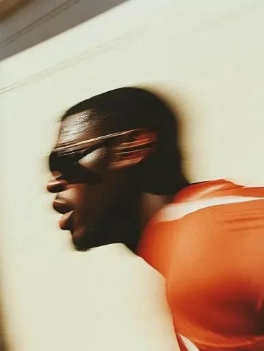 A person with dark skin wearing sunglasses and an orange top, captured in a side profile with motion blur.