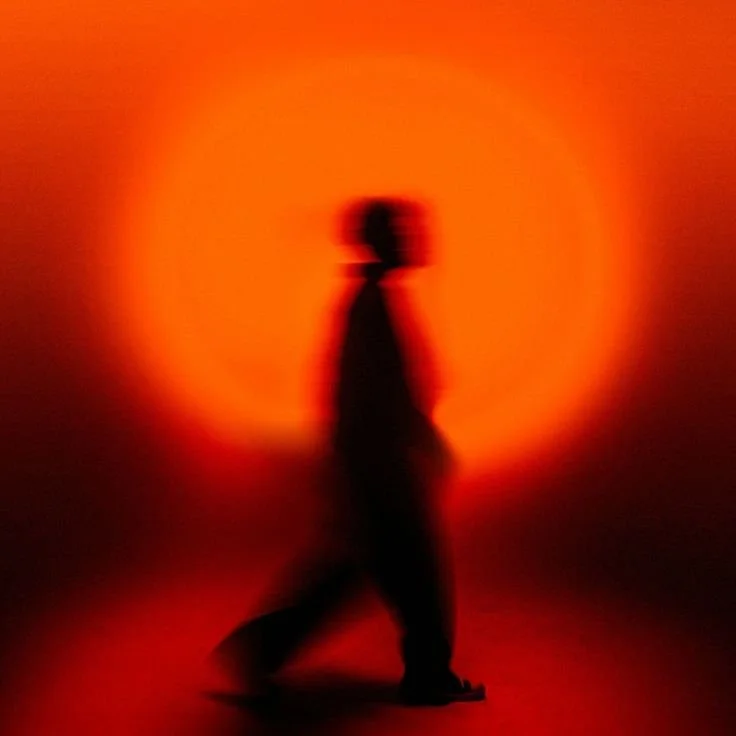 A blurred silhouette of a person walking with a red and orange background.