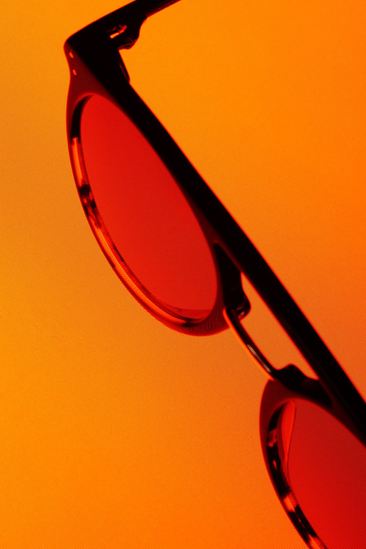 Close-up of sunglasses with orange-tinted lenses on an orange background.