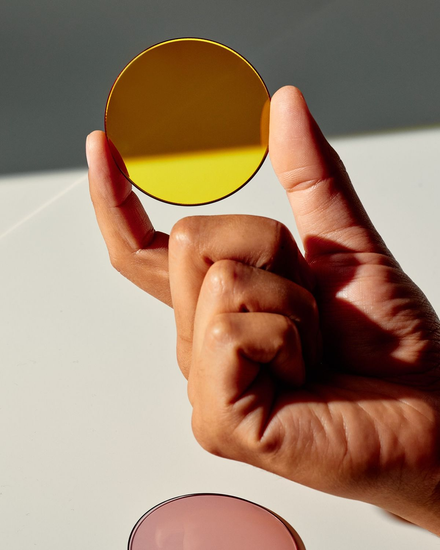 Person holding a yellow-tinted circular lens or filter between their thumb and index finger