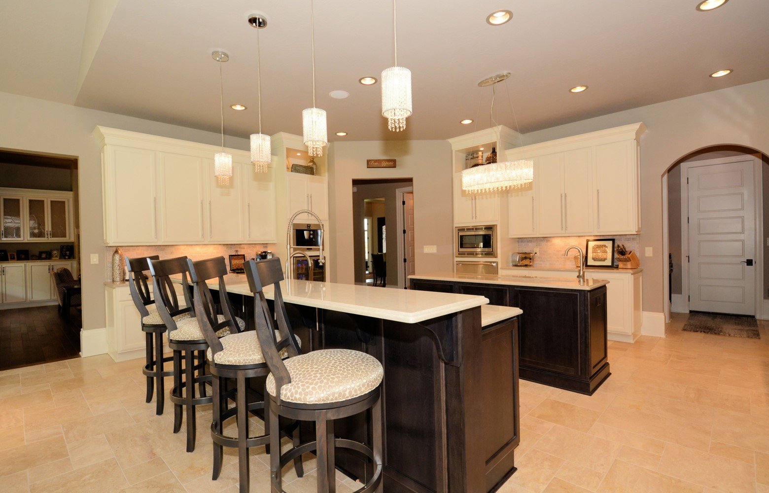 A spacious kitchen with an island, four chairs, white cabinets, and modern appliances, illuminated by multiple pendant lights.