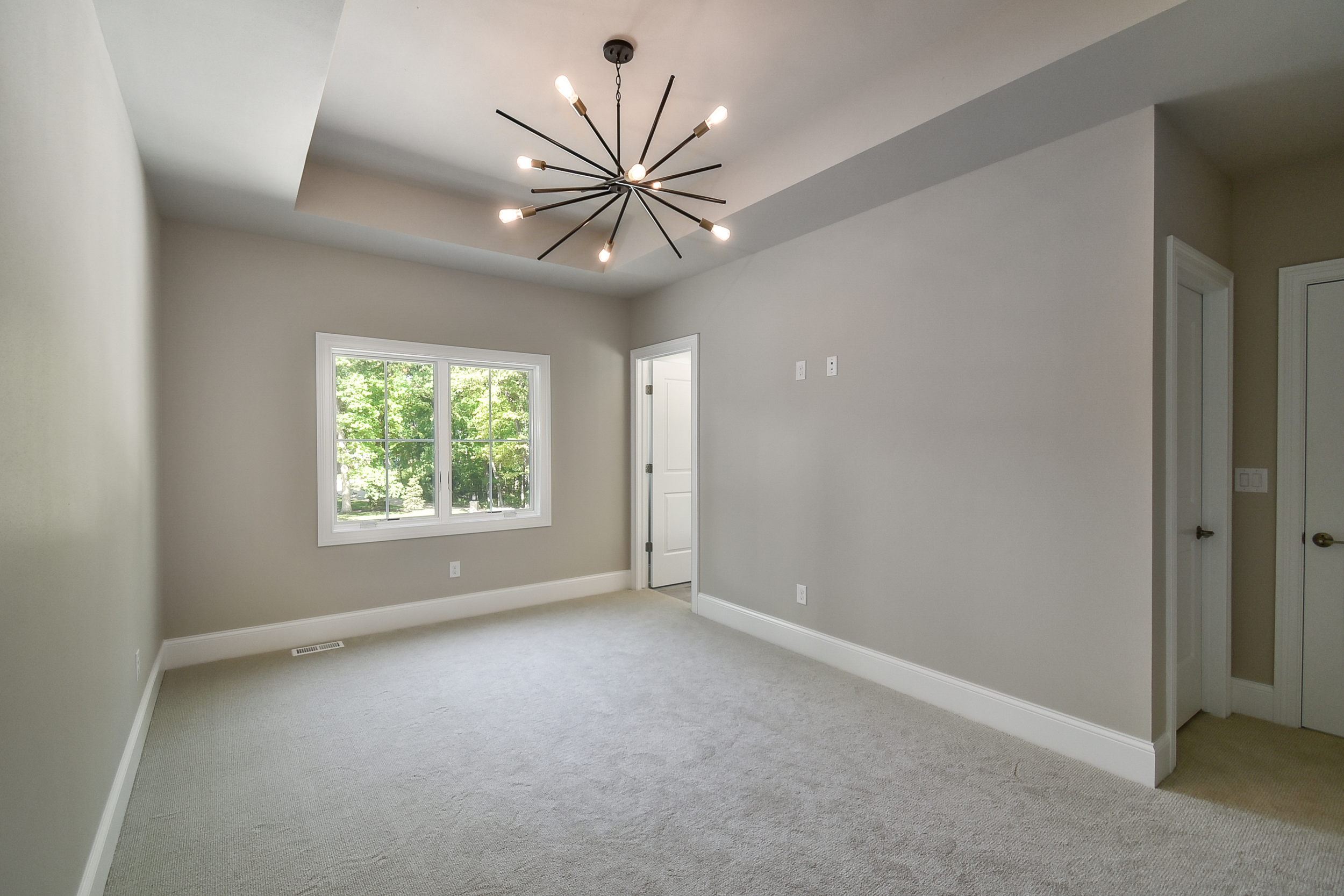 Empty living room with large window, ceiling light fixture, beige walls, and carpeted floor.