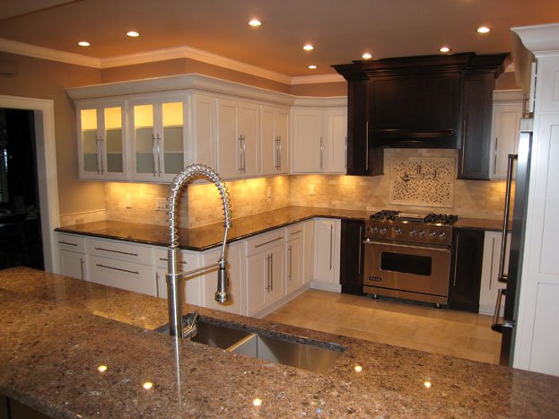 Modern kitchen with white cabinets, granite countertops, stainless steel sink, black range hood, and stainless steel stove.