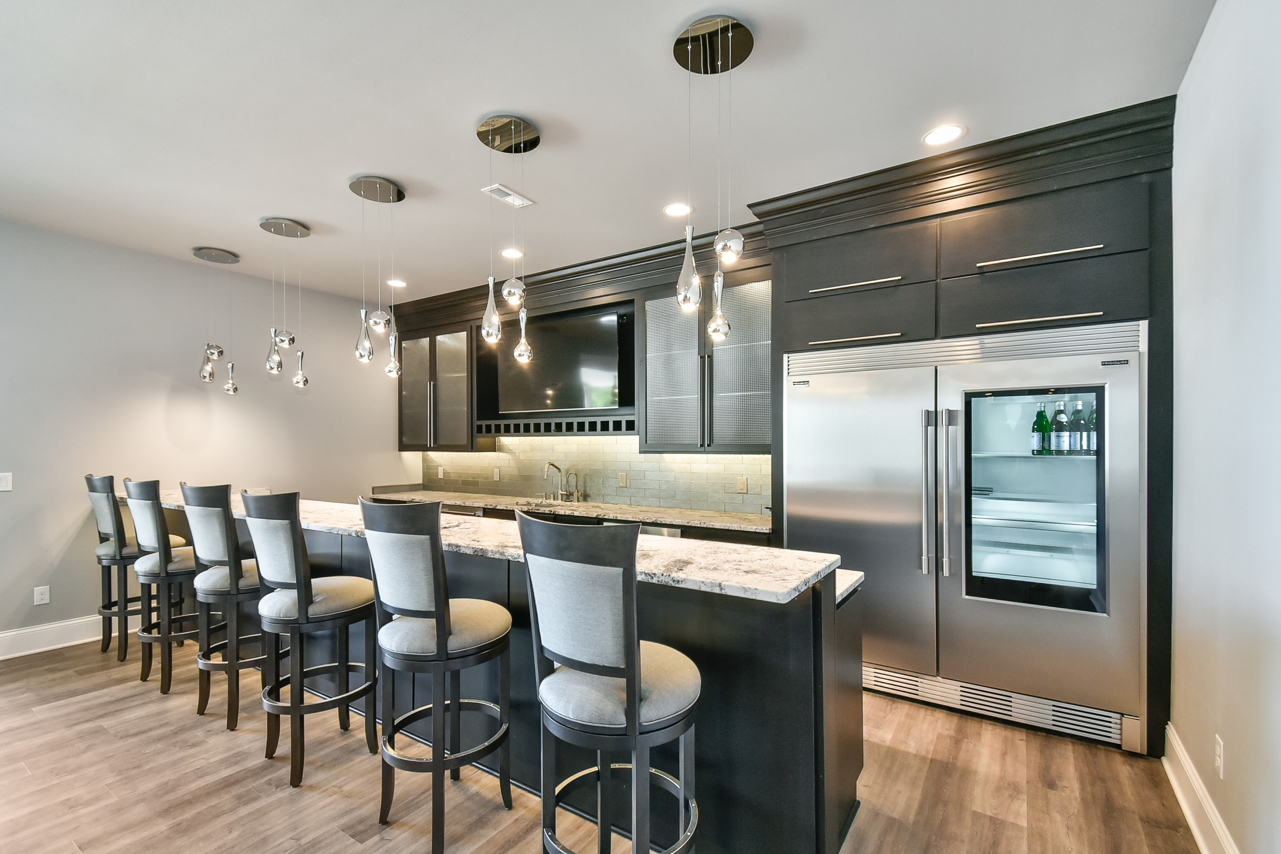 Modern kitchen with black cabinets, a marble island, a built-in wine fridge, and a ceiling with decorative hanging pendant lights.
