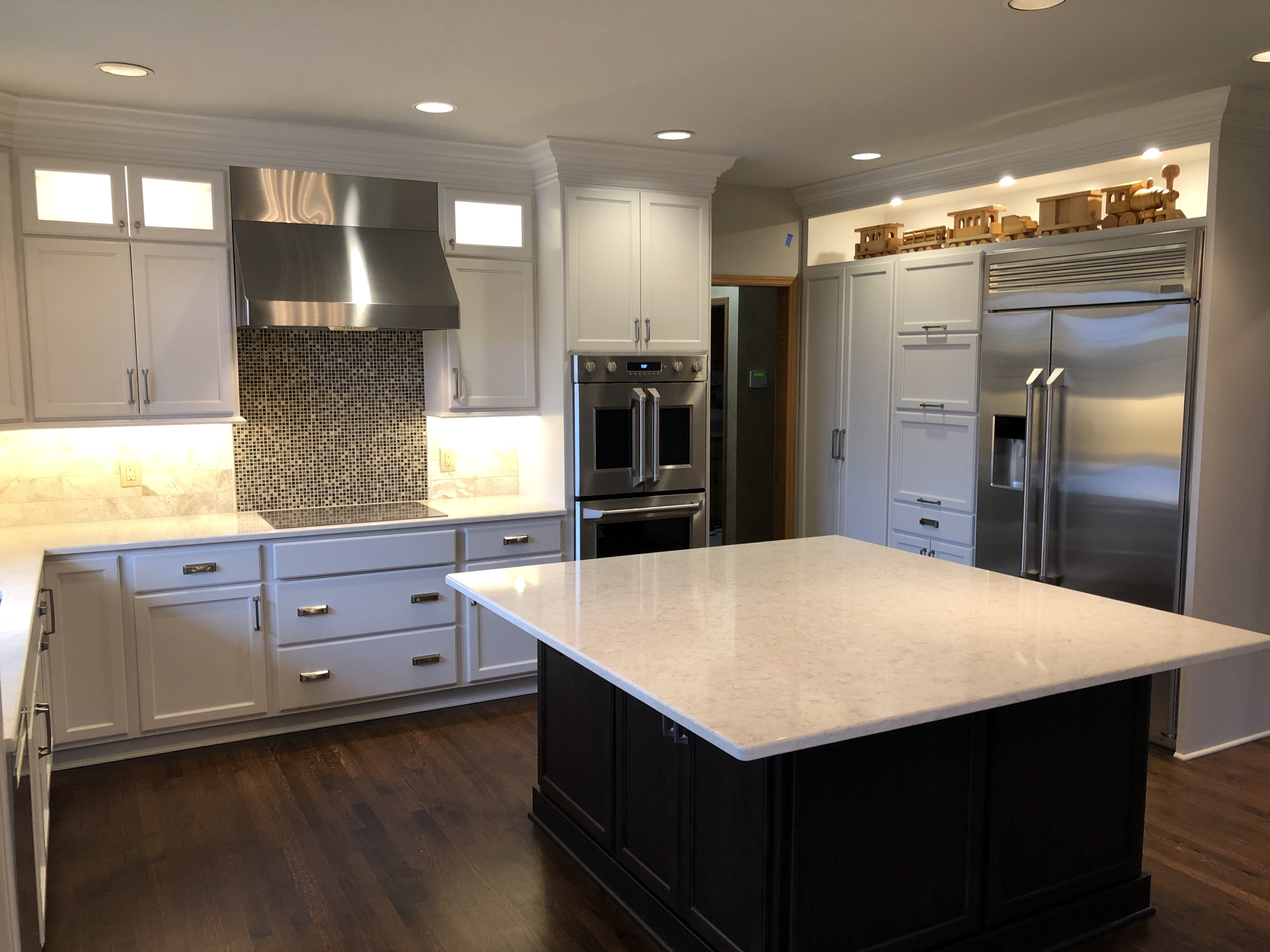 Modern kitchen with white cabinets, stainless steel appliances, and a large central island with a dark base and white countertop.