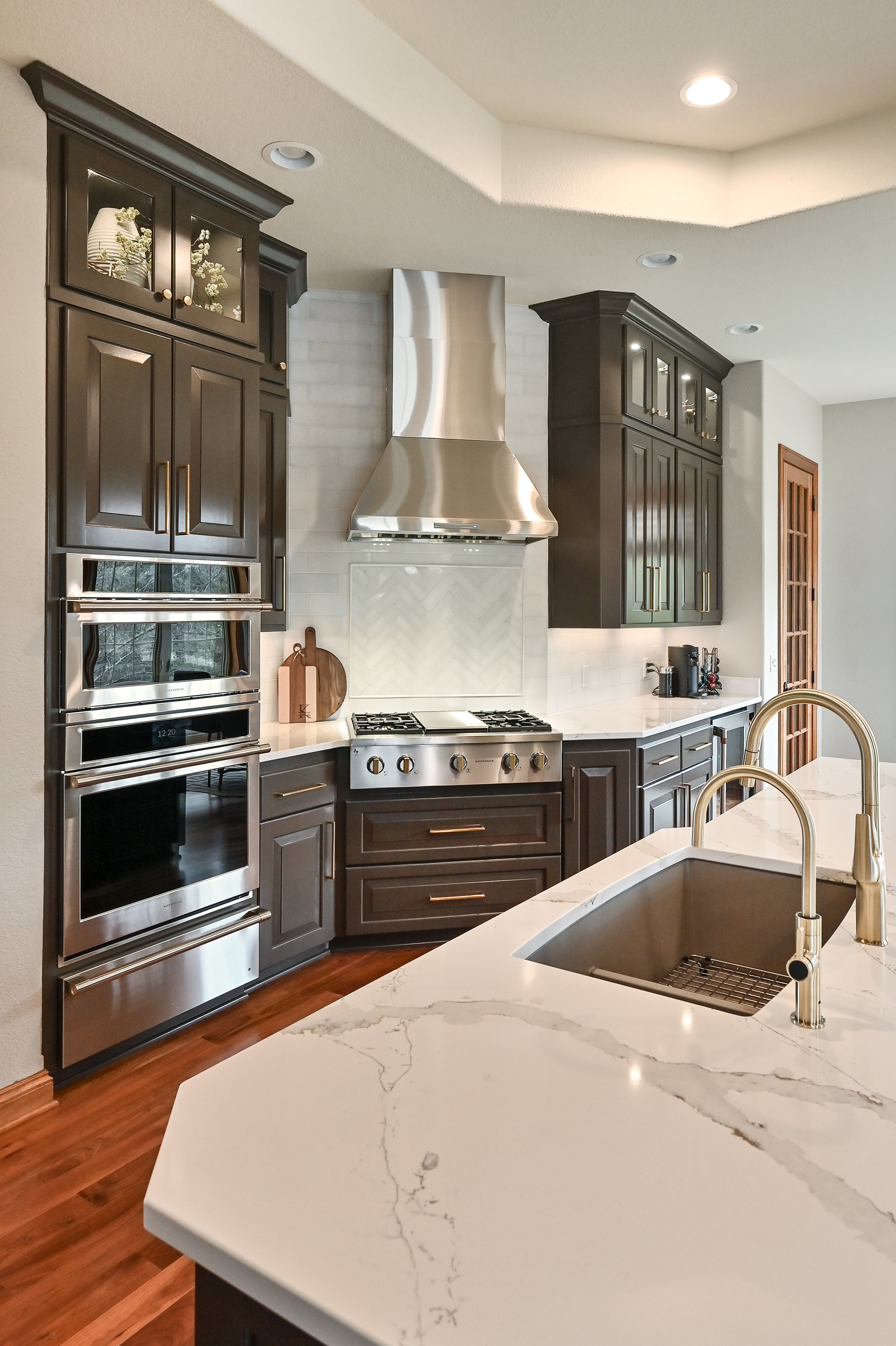 Modern kitchen with dark wood cabinets, white marble countertops, stainless steel appliances, a vent hood, and a white tiled backsplash.