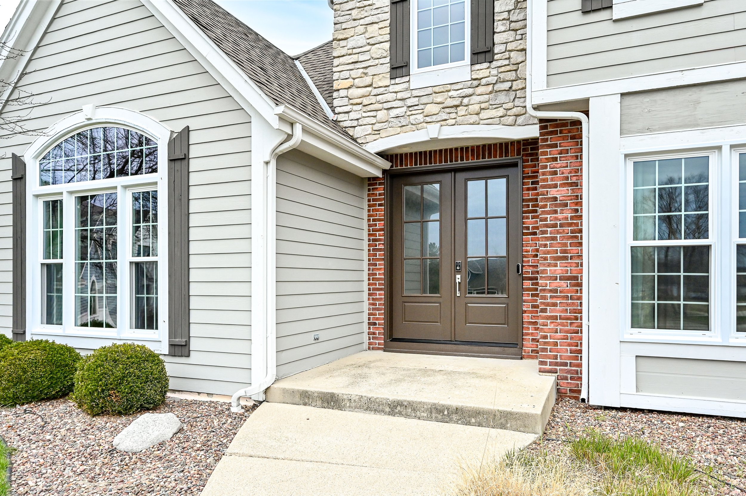 Front entrance of a house with a double door, brick and stone exterior, and multi-pane windows.