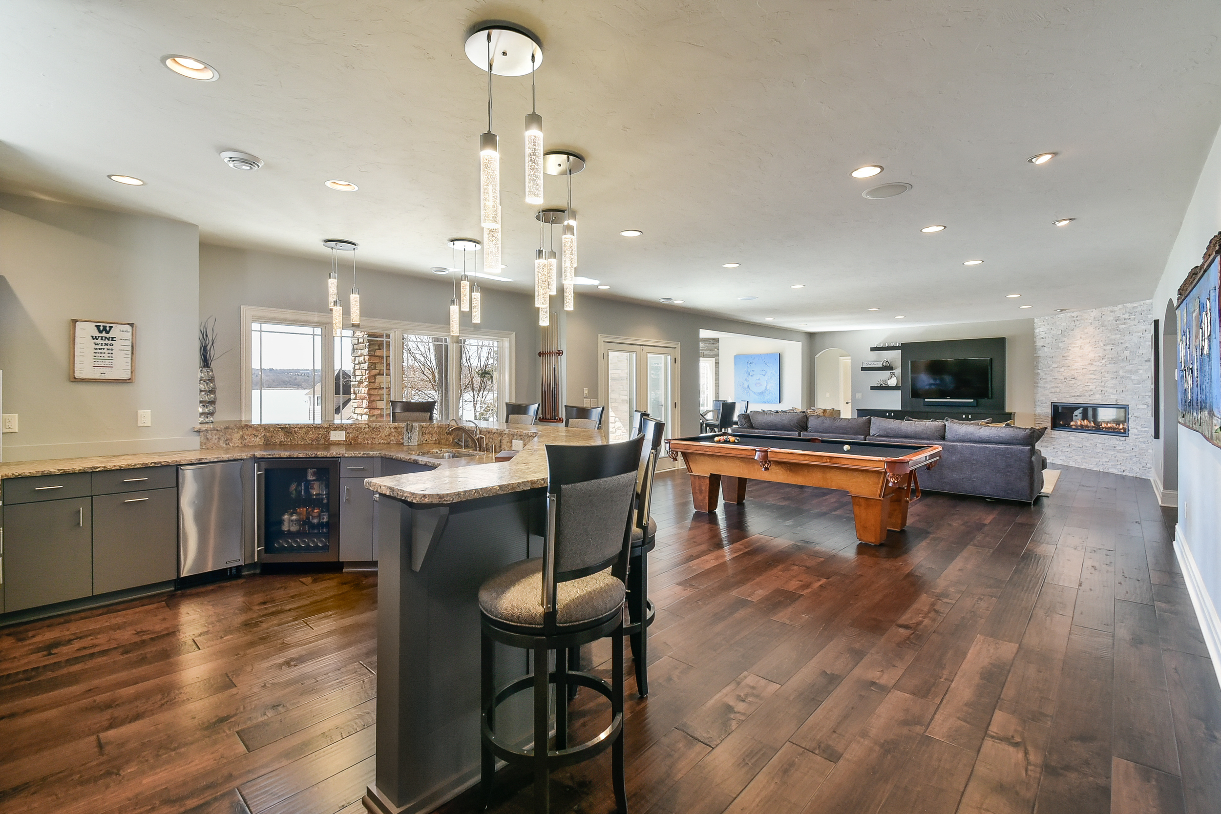 Open-concept living room and kitchen with hardwood floors, modern lighting fixtures, granite countertops, and a pool table.