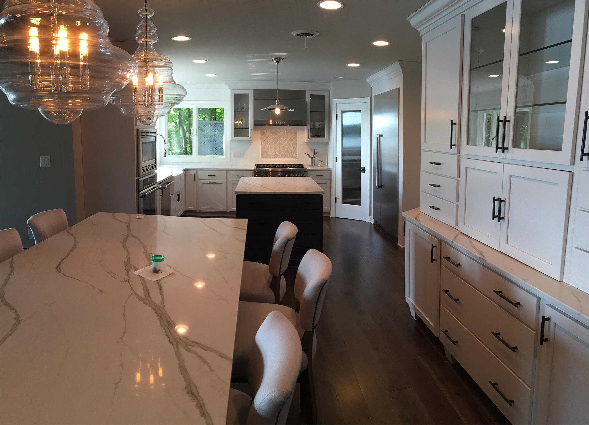 Modern kitchen with white cabinets, marble island, dark hardwood flooring, and pendant lighting.
