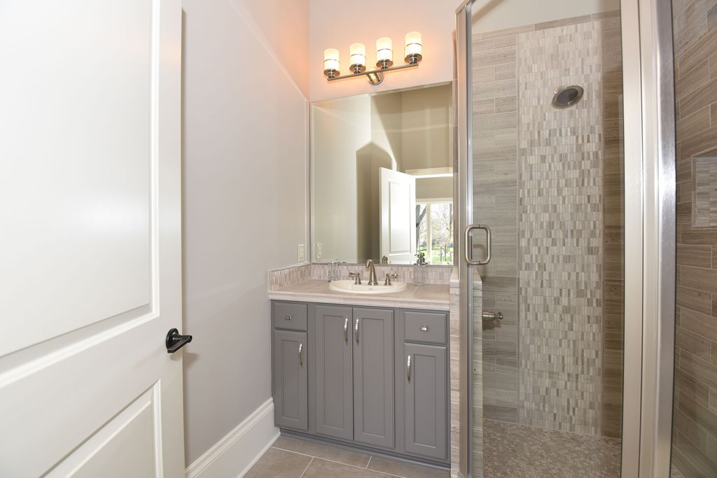 Bathroom with a gray vanity, a large mirror, and a walk-in shower with glass door and tiled walls.