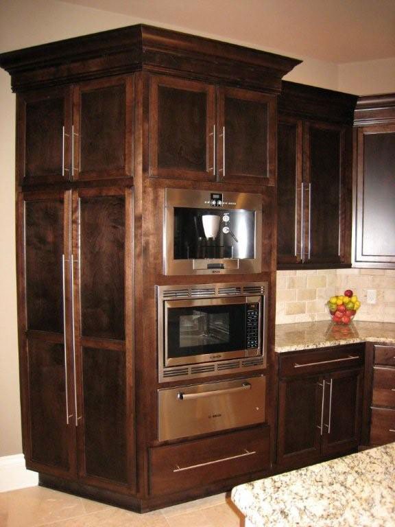 Kitchen with dark wood cabinets, built-in microwave, and oven, located next to a brick backsplash and granite countertop, with a bowl of apples on the counter.