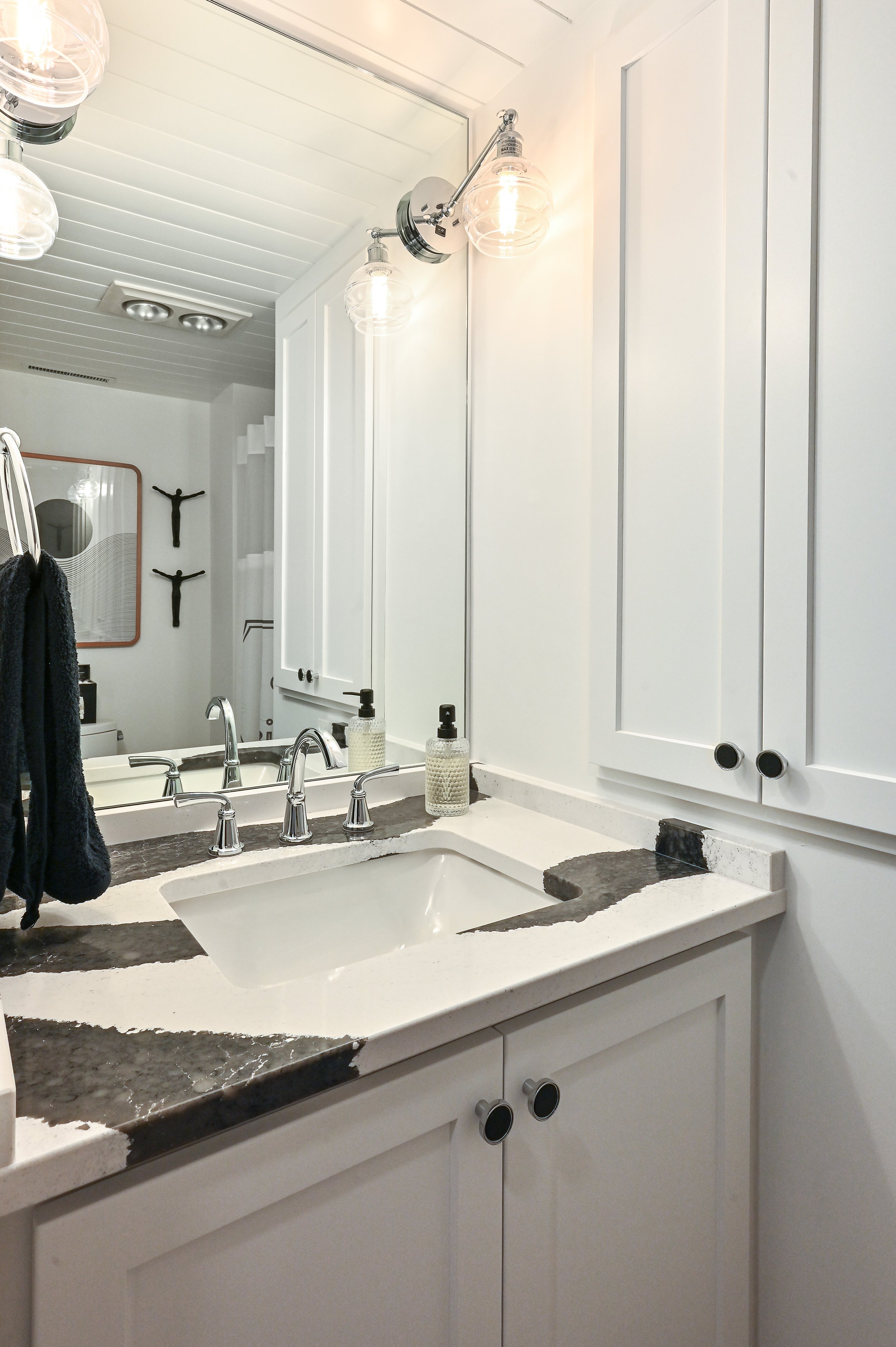 Bathroom sink with white cabinets, a marble countertop with black and white pattern, a large mirror, and modern fixtures. There are two soap dispensers on the counter and a towel hanging on a hook.