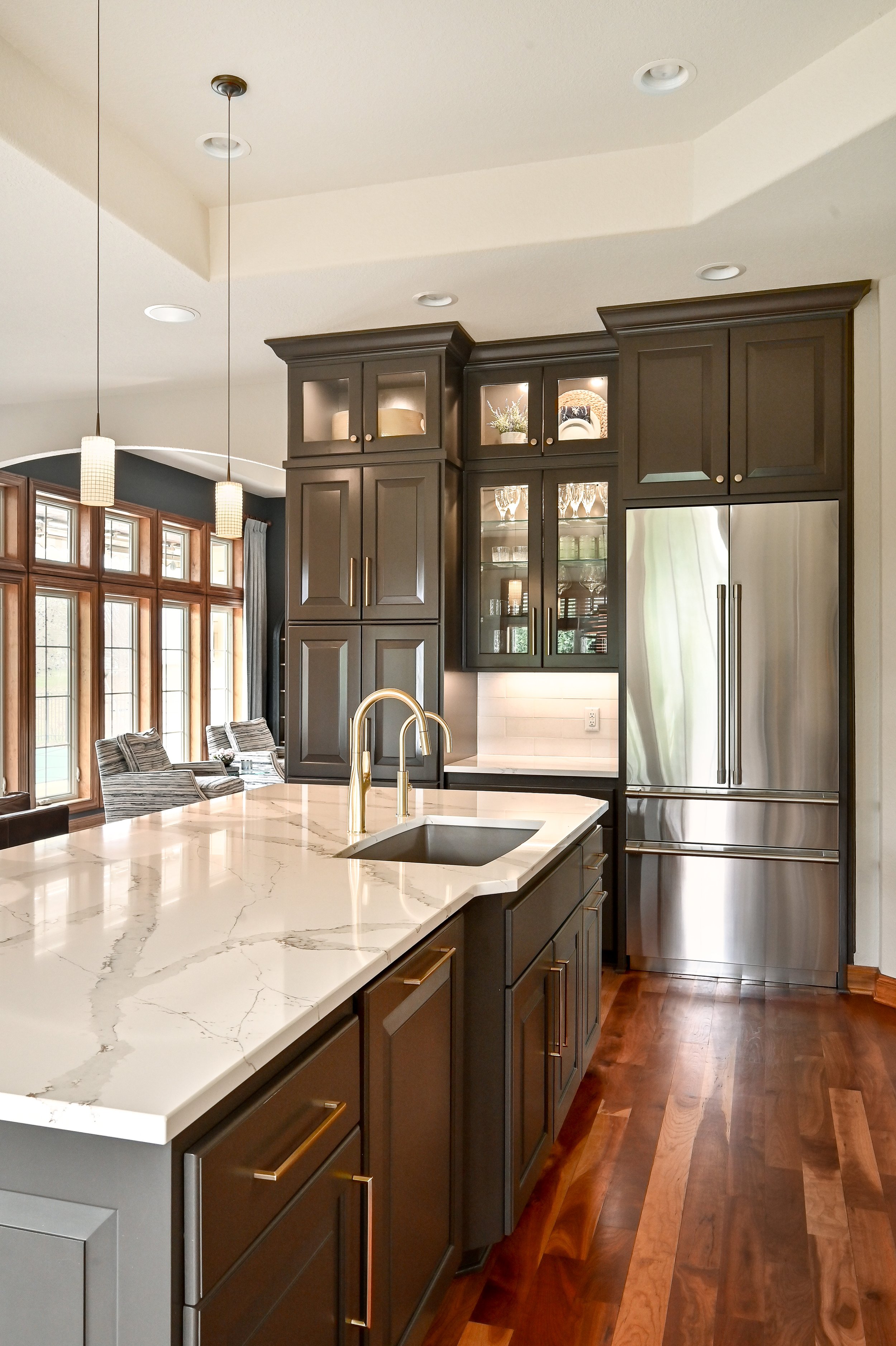 Modern kitchen with dark cabinets, white marble countertop, stainless steel fridge, and wooden flooring.