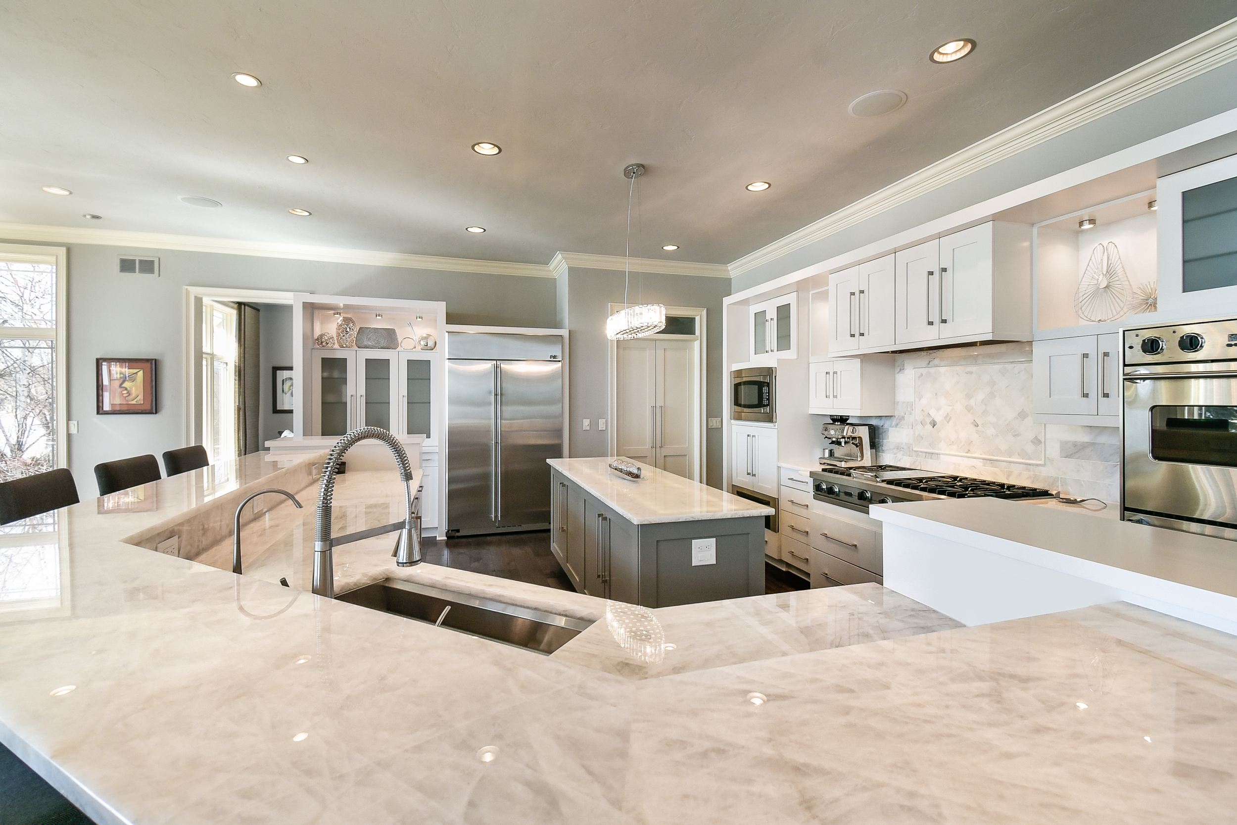 Modern kitchen with white cabinets, marble countertops, stainless steel appliances, and a central island with a sink and faucet.