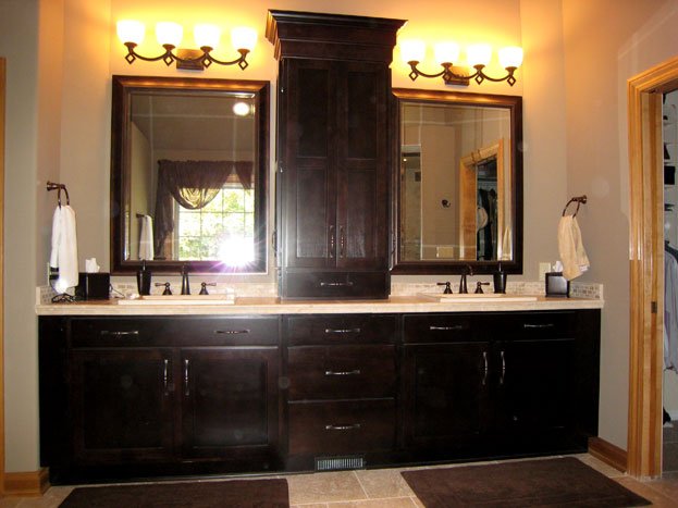 Bathroom vanity with two mirrors, dark wood cabinets, two light fixtures, and a window reflected in the mirrors.