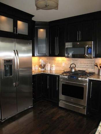 Modern kitchen with black cabinets, stainless steel refrigerator, oven, microwave, and white brick backsplash.