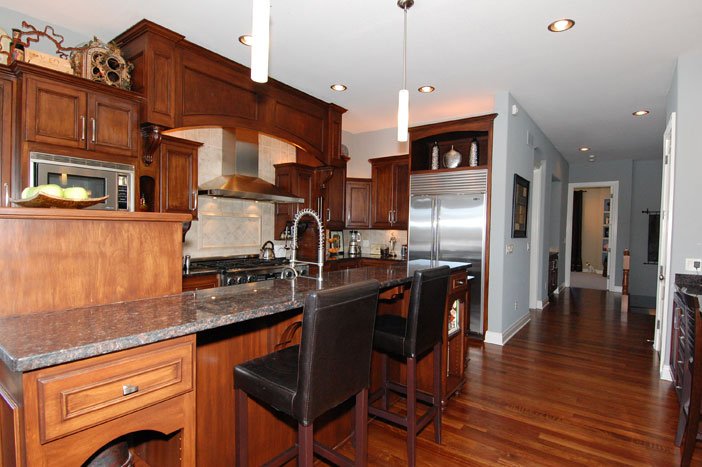 Kitchen with wooden cabinets, granite countertop, stainless steel appliances, and two black bar stools at the counter. There are pendant lights hanging from the ceiling.