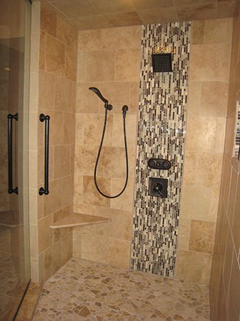Tile shower with glass door, built-in seat, handheld showerhead, and mosaic tile accent wall.
