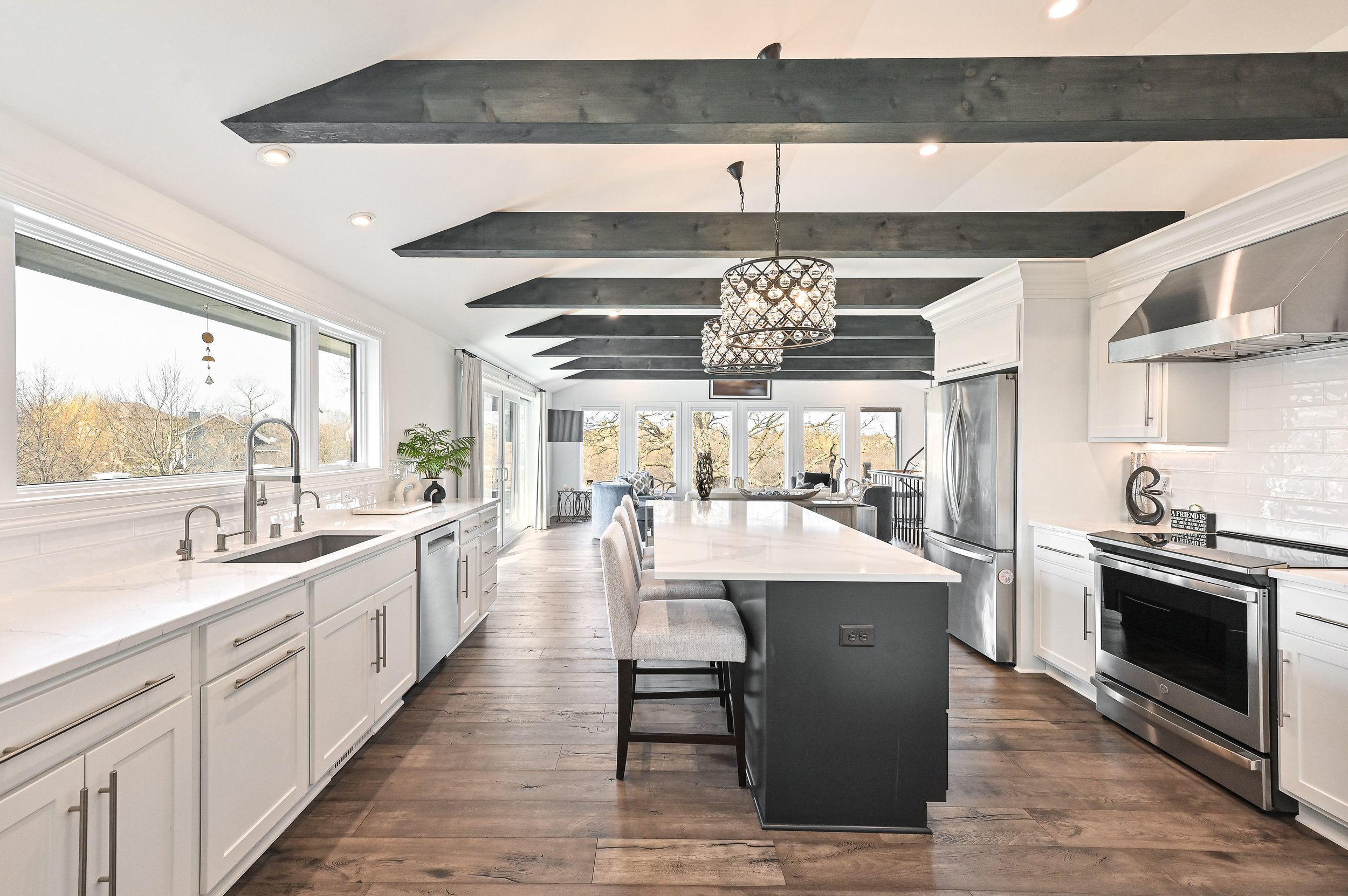 Modern kitchen with white cabinetry, island with seating, stainless steel appliances, and large windows overlooking trees.