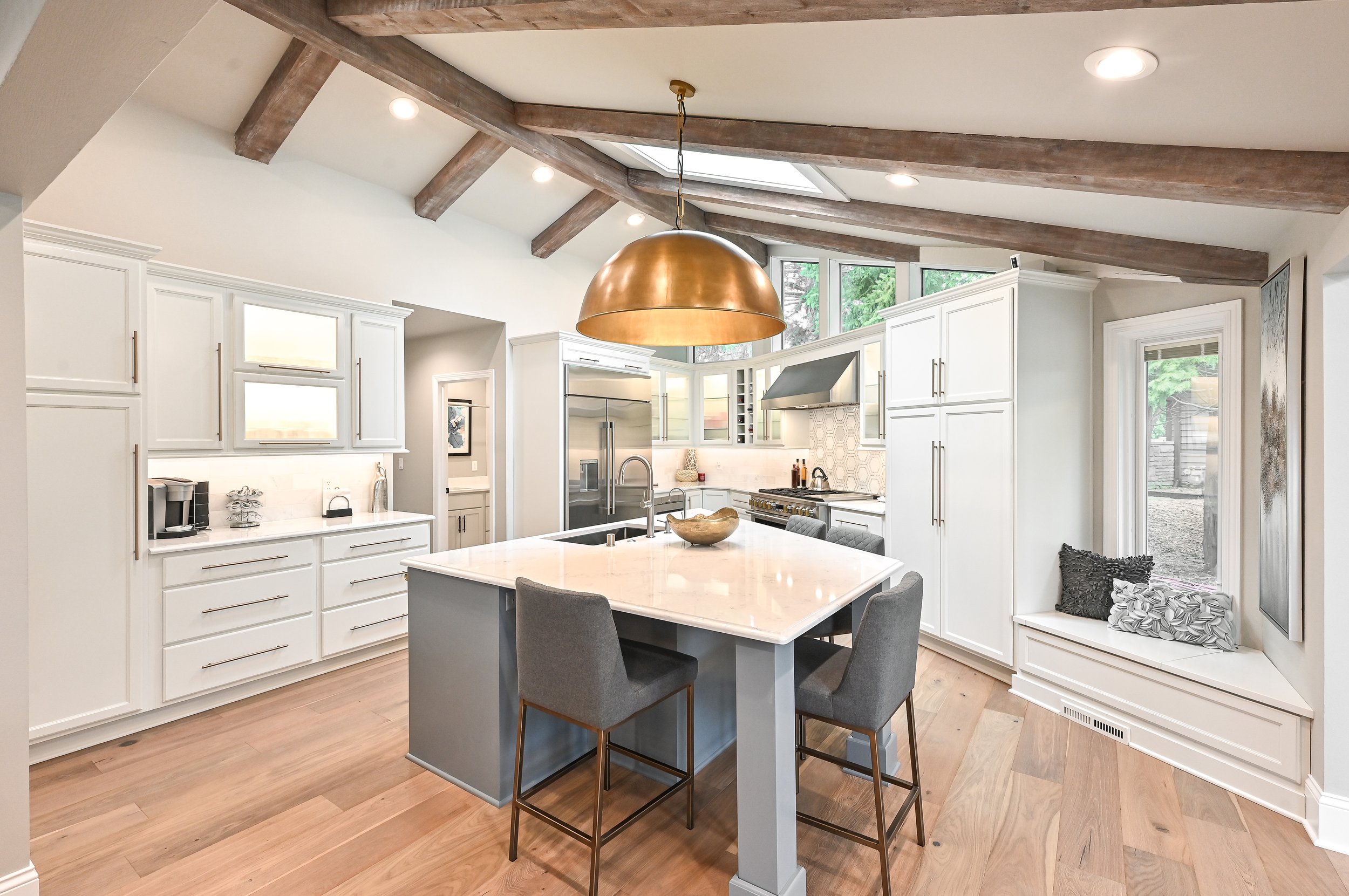 Modern kitchen with white cabinets, marble island, and wooden ceiling beams.
